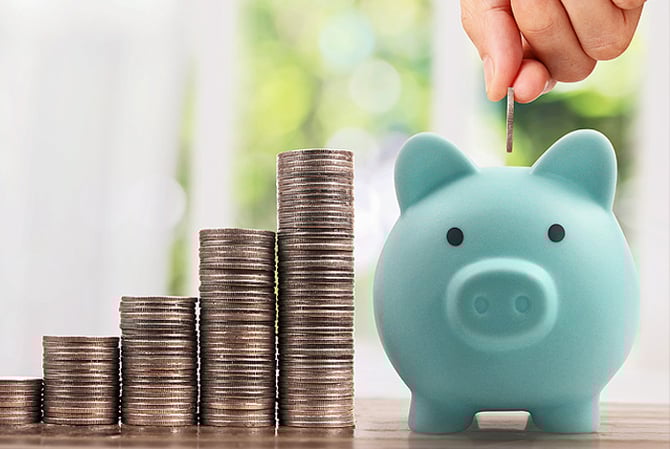 Uma pilha de moedas em formato de escadinha ao lado de um cofrinho azul no formato de porquinho, onde uma mão está depositando uma moeda, representando a previsibilidade que as empresas podem ter ao adotar o pagamento recorrente através da solução Assinaturas do Mercado Pago.