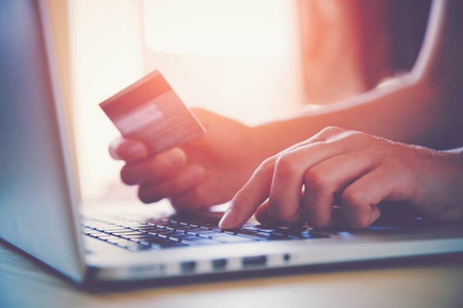 Mãos de uma pessoa mexendo no laptop e segurando um cartão de crédito para preencher a página de Checkout Pro do Mercado Pago e assim concluir sua compra em uma loja digital