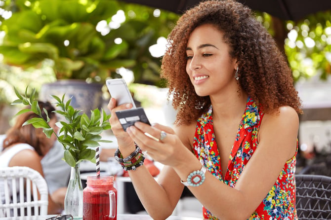 Mercado Pago: Mulher sentada em mesa de restaurante com cartão e celular em mãos representando os consumidores digitais 