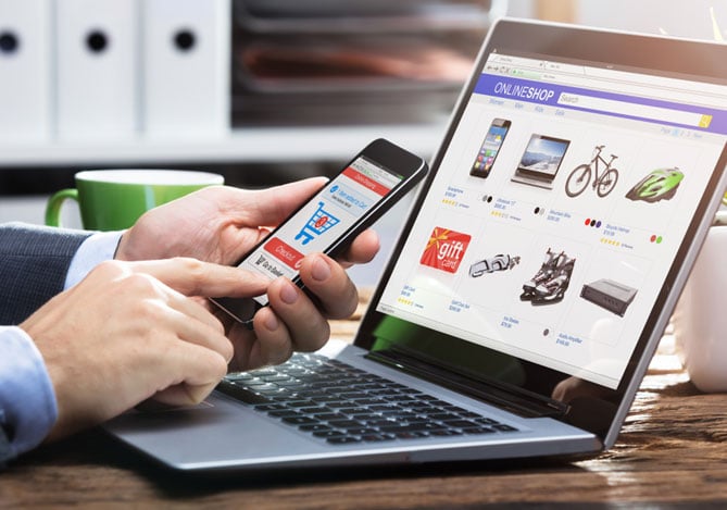 Mãos de uma pessoa mexendo no celular enquanto o laptop está aberto em um e-commerce para identificar formas de prevenir a contestação de compra ou chargeback com a ajuda do Mercado Pago