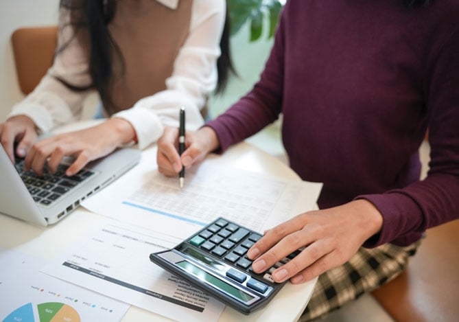 Mercado Pago: imagem de duas pessoas, uma à frente de um notebook e outra usando uma calculadora para fazer análises e evitar impactos negativos de uma crise financeira.