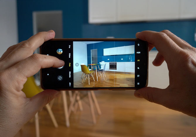 Mercado Pago: imagem de duas mãos segurando um celular. Pela tela do celular é possível ver a imagem de uma cozinha para uma produção de fotografia de arquitetura. Na imagem da tela do celular há também  uma mesa com duas cadeiras.