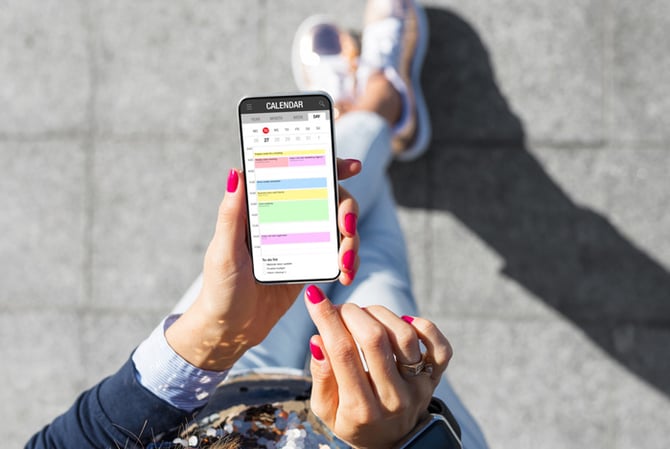 Mercado Pago: pessoa vista de cima, com celular na mão. A tela está aberta na agenda tributária, onde há diversos lembretes coloridos. 
