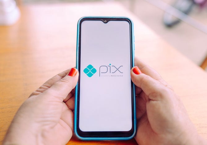 Imagem de mãos segurando um celular com o logo do Pix na tela, representando um celular que já possui o pagamento via Pix por aproximação ativado para realizar pagamentos nas maquininhas Point Mercado Pago com essa tecnologia.