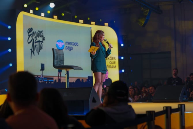 A cantora Anitta vestindo as cores do Mercado Pago no palco do Mercado Livre Experience durante a sua palestra, falando sobre o banco digital Mercado Pago ser um dos patrocinadores dos Ensaios da Anitta em 2025