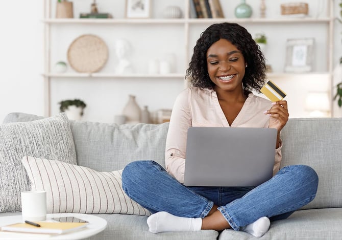 Mercado Pago: Mulher sentada no sofá com um cartão de crédito na mão e laptop no colo adquirindo o cashback no e-commerce