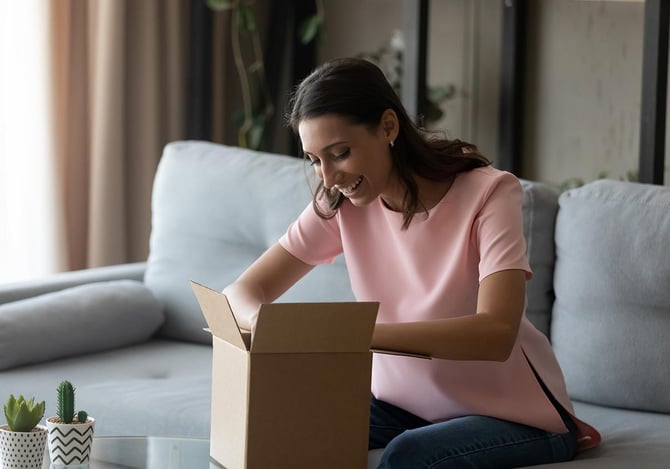 Mulher sorrindo enquanto abre uma caixa de papelão