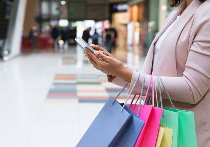 Link de pagamento Mercado Pago para venda online: mulher segurando sacolas de compras em uma mão e celular na outra.