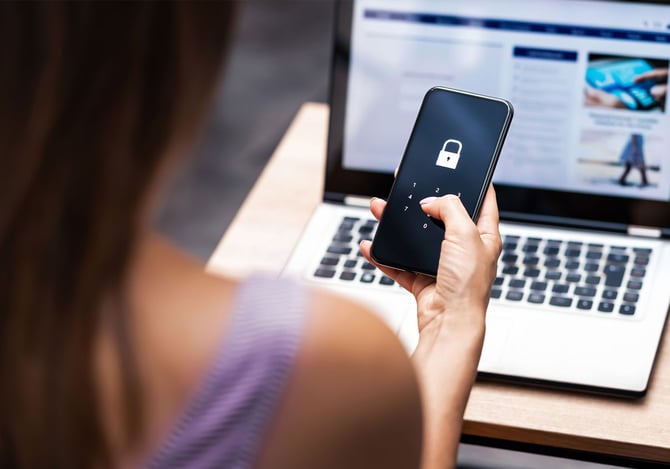 Mulher segurando celular com senha em frente ao computador