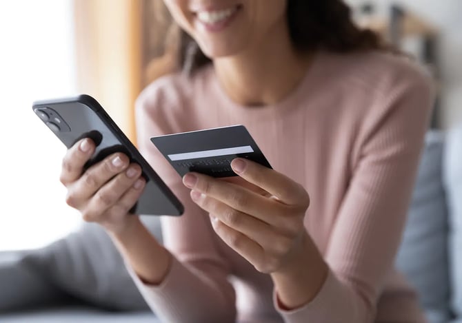 Mulher sorrindo e digitando os dados do cartão de crédito no smartphone com ajuda do Mercado Pago para potencializar sua segurança digital