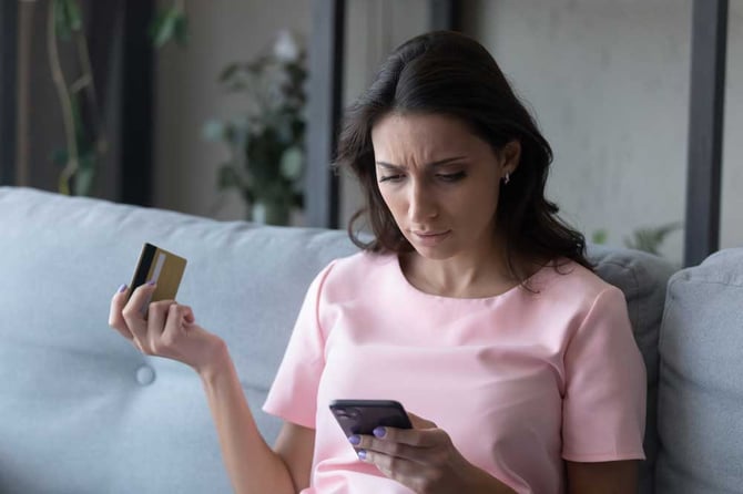 Mercado Pago: Consumidora assustada olhando o celular com um cartão de crédito na mão preocupada com fraudes no e-commerce.