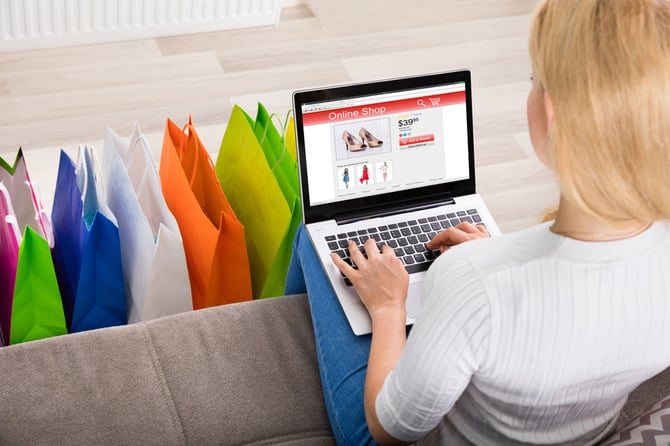 Mulher fazendo compras pelo computador com várias sacolas a seus pés