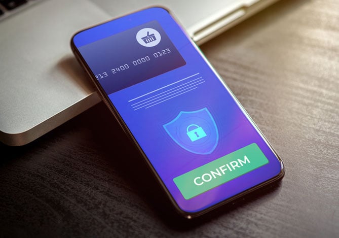 Mercado Pago: imagem de um celular apoiado sobre um notebook aberto, no qual é possível ver uma imagem ilustrativa de um processo de pagamento seguro, com um cartão virtual na tela e um botão verde com o texto “confirm” (confirmar).
