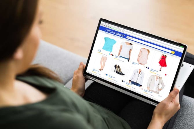 Consumidora com notebook no colo escolhendo roupas no e-commerce para parcelar com as soluções “compre agora, pague depois”. 