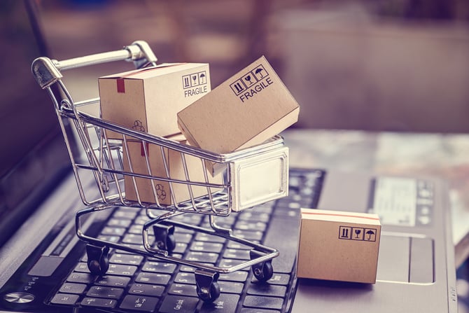 Imagem de um carrinho de compras com caixas em cima do teclado de um laptop sugerindo compras online e todo o processo de taxa de aprovação no e-commerce
