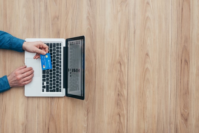 Imagem de um laptop aberto no chão com a mõo de uma pessoa em cima segurando o cartão de crédito para entender como funciona a multiadquirência Mercado Pago