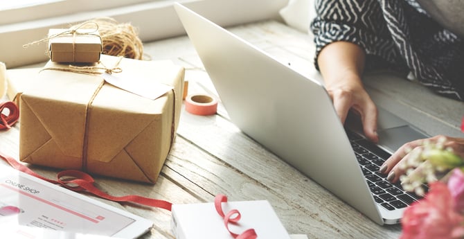 Uma pessoa mexendo em um computado em uma mesa com caixas de presente