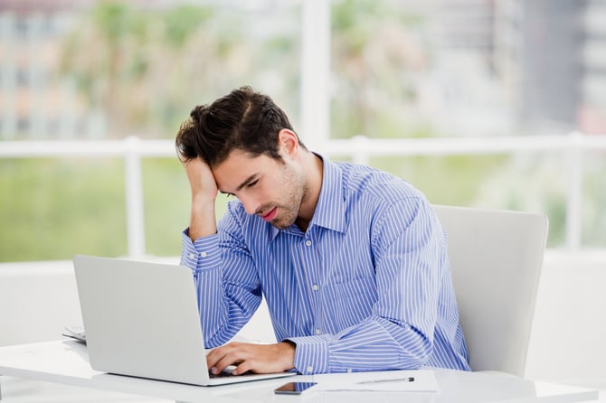 Mercado Pago: Homem com camisa azul sentado em mesa de escritório com computador aberto pesquisando sobre chargeback no e-commerce