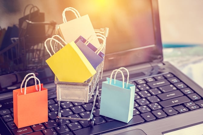 Um laptop aberto com vários mini sacolas de compra e carrinho sugerindo a experiência no checkout Mercado Pago