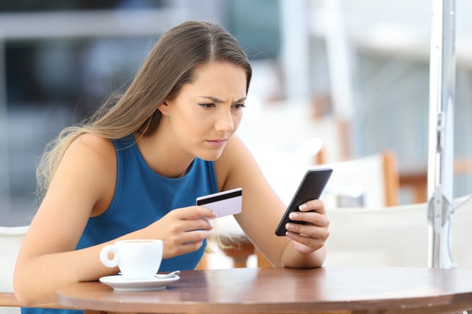 Mercado Pago: Mulher com regata azul, sentada em mesa com celular e cartão na mão buscando sobre a tecnologia Machine learning. 