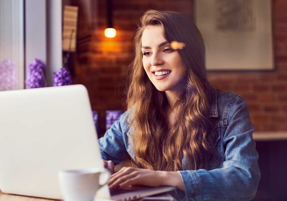 Mercado Pago: Mulher de camisa jeans sentada em frente ao notebook tendo uma experiência positiva em um processo de pagamento online