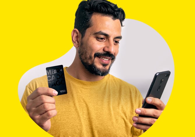 Mercado Pago: homem com um celular em uma mão e o cartão empresarial do Mercado Pago em outra mão.