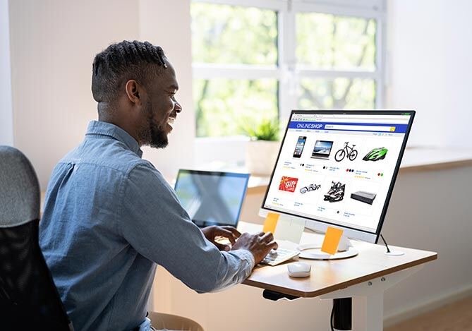 Homem de camisa azul sentado em mesa de escritório, em frente ao computador implementando o checkout transparente em seu e-commerce com comércio combinável.