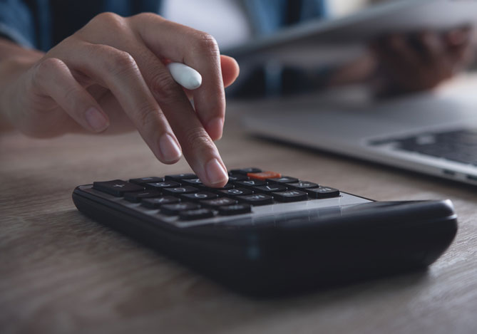 Mercado Pago: imagem de uma pessoa digitando números em uma calculadora enquanto mexe em um notebook para avaliar as condições de empréstimo Mercado Pago.