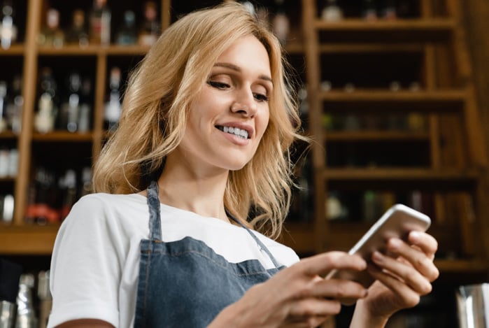 Mercado Pago: mulher de avental no seu bar mexendo no celular para enviar um link de Pagamento recebimento na hora