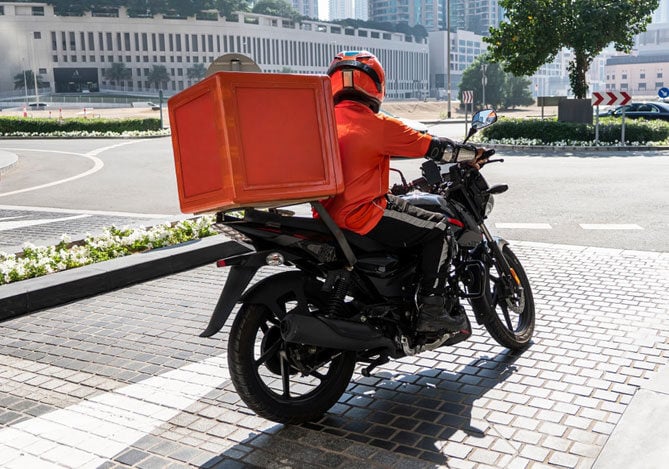 Mercado Pago: imagem de um motoboy em cima da moto com um baú de entregas, vestindo roupa vermelha, simulando a saída para deixar um pedido o qual terá o pagamento realizado usando a melhor maquininha de cartão.