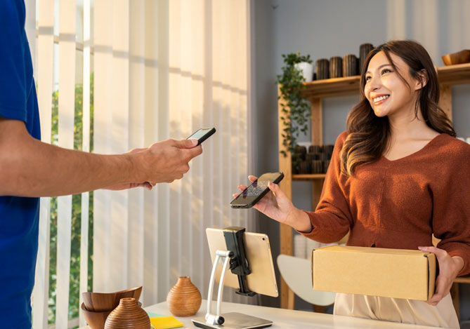Mercado Pago: mulher com celular em uma mão e caixa em outro fazendo o pagamento digital ao vendedor que está na sua frente.
