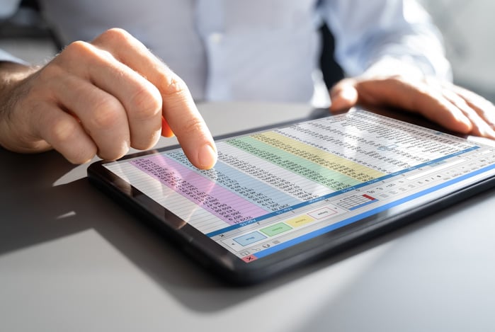 Mercado Pago: mãos de um homem mexendo em um tablet com uma planilha de gastos empresariais na tela. 