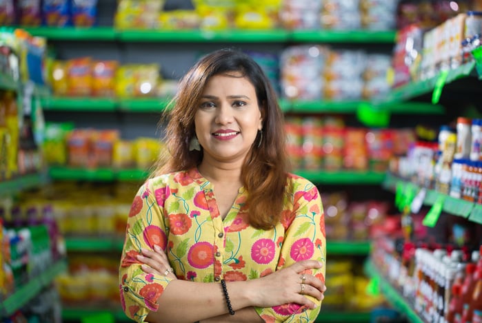 Mercado Pago: mulher de braços cruzados, sorrindo para a câmera, em uma mercearia com inúmeros produtos, representando seu ponto de venda.