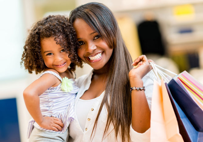 Mercado Pago: imagem de uma mulher com uma criança em seu colo, ambas estão sorrindo. Em uma das mãos, a mulher segura sacolas, indicando a realização de compras a partir de um programa de fidelidade.