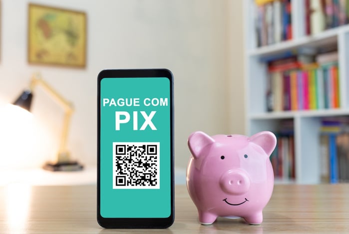 Mercado Pago: um porquinho para depósito de moedas ao lado de um celular com o Pix QR Code aberto e a frase “pague com Pix” para quem deseja escanear o código. 