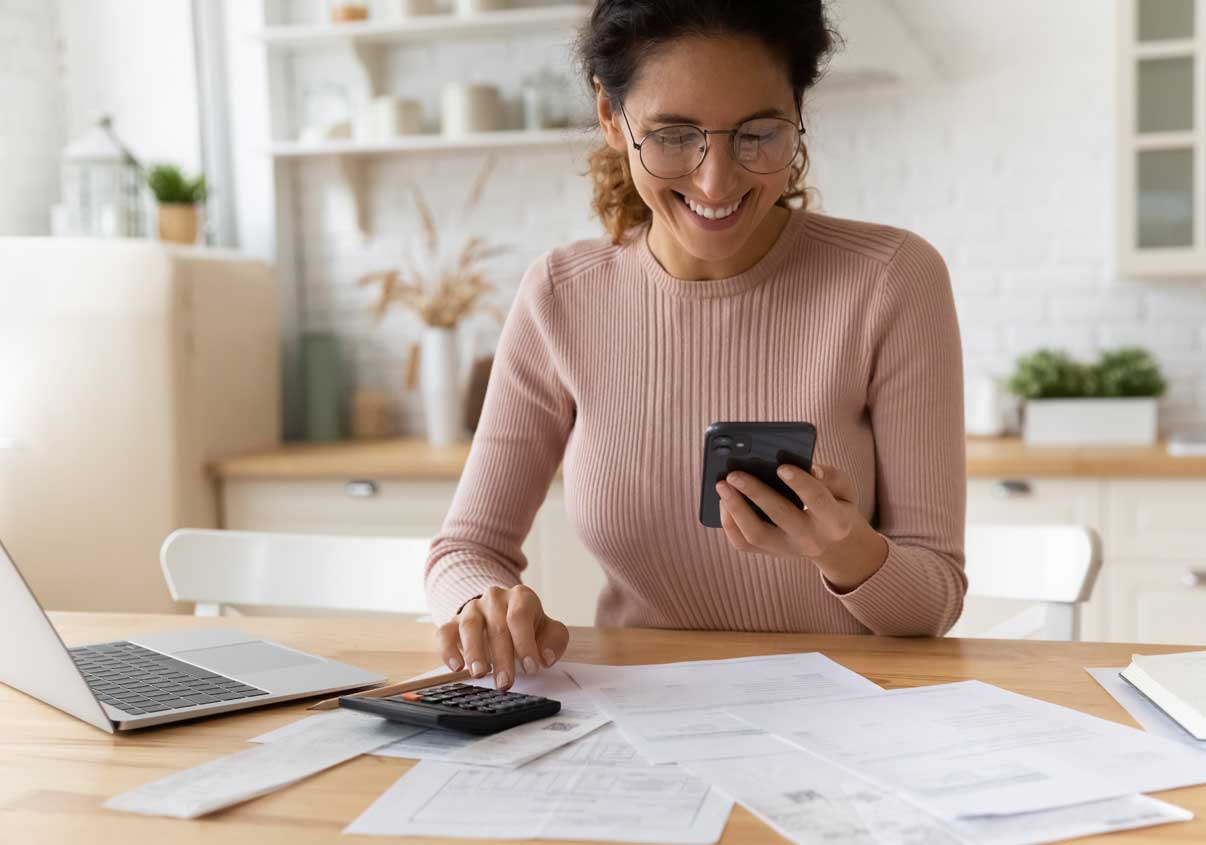 Mulher sorrindo para o celular próxima a uma mesa com calculadora