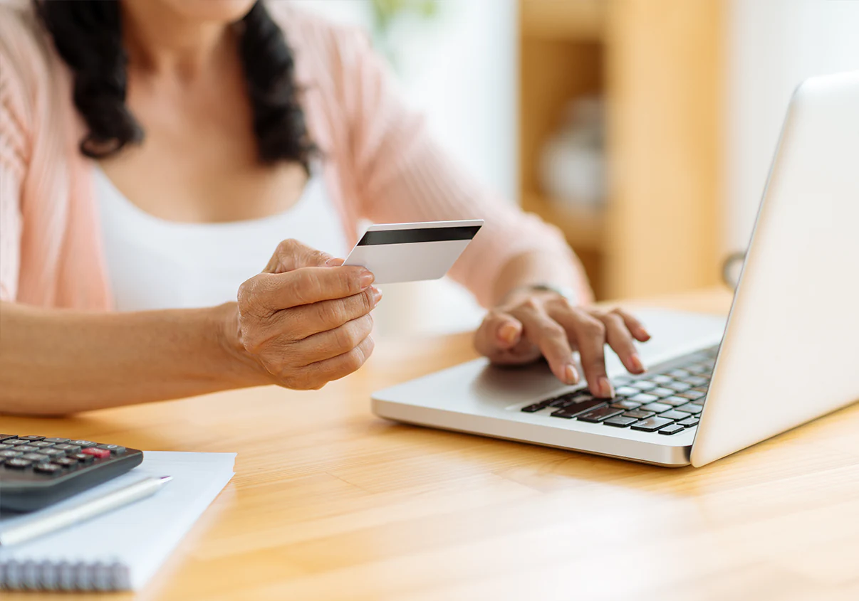 Mulher segurando cartão de crédito enquanto digita seus dados no laptop