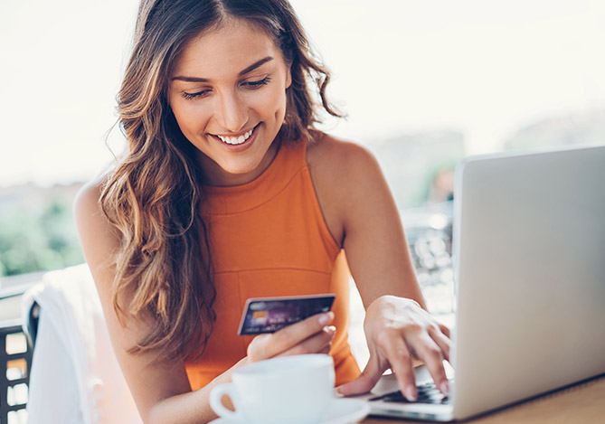 Mulher de roupa laranja segurando um cartão de crédito, usando um notebook para elevar a taxa de conversão da plataforma de ecommerce com Mercado Pago
