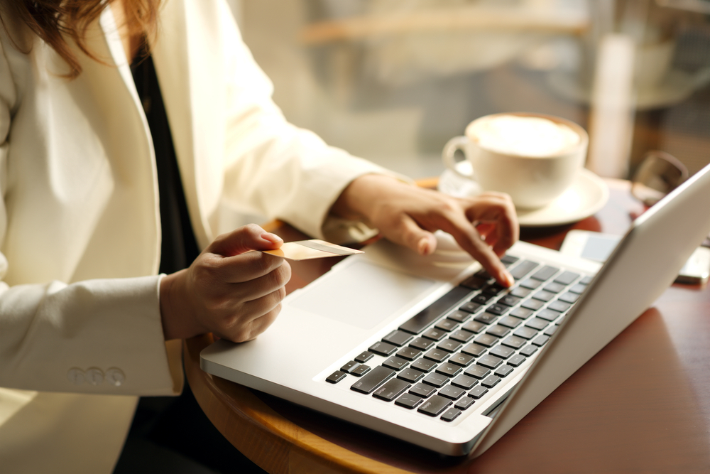 Mãos de mulher com paletó branco, digitando em um notebook com Checkout Pro Mercado Pago  e xícara de café apoiada na mesa. 