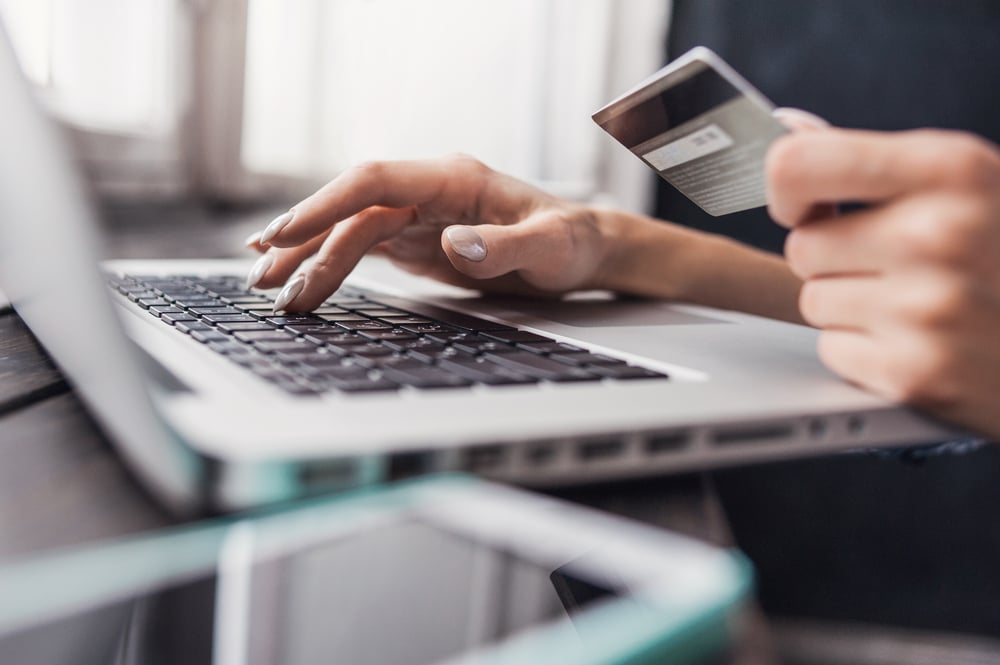 Mãos de uma pessoa, sendo que uma está mexendo em um laptop e a outra está segurando um cartão de crédito para efetuar o pagamento de sua compra no Checkout do Mercado Pago